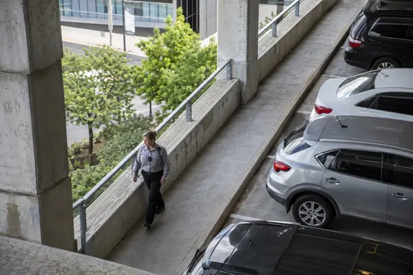 Illustrative private security work in Little Rock, Arkansas: Woman in grey long-sleeve uniform shirt patrolling public-facing corporate parking structure