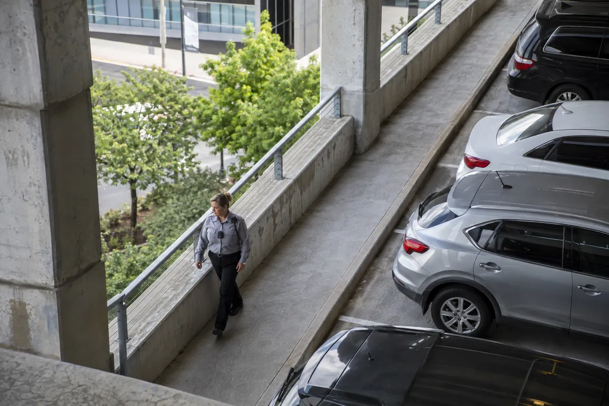 Illustrative private security work in Little Rock, Arkansas: Woman in grey long-sleeve uniform shirt patrolling public-facing corporate parking structure