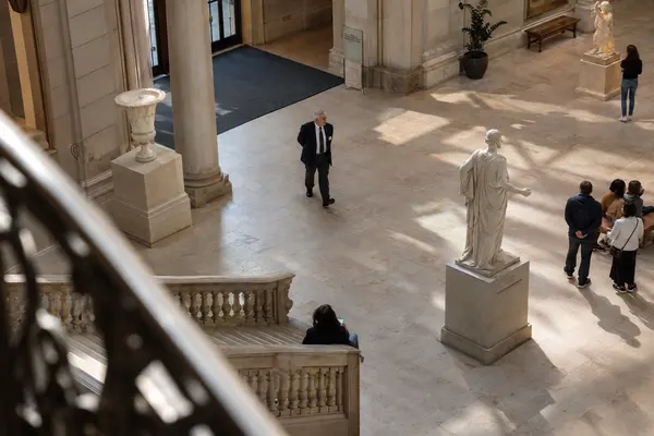 Illustrative private security work in Philadelphia, Pennsylvania: Older white male security officer in navy blazer and white shirt patrolling an airy museum atrium in Philadelphia.