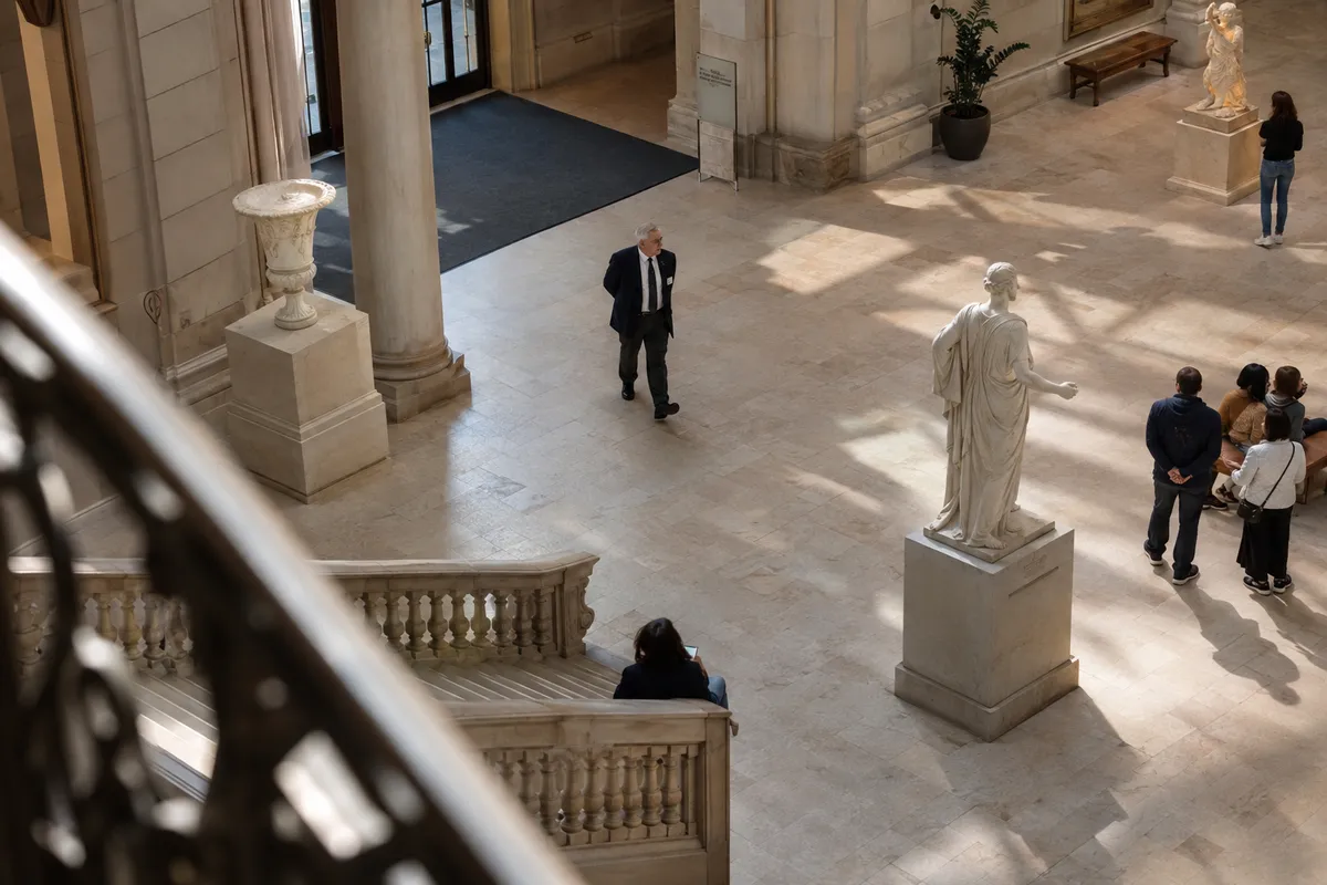 Illustrative private security work in Philadelphia, Pennsylvania: Older white male security officer in navy blazer and white shirt patrolling an airy museum atrium in Philadelphia.